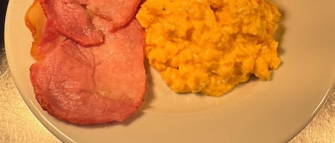 A plate with ham and scrambled eggs on a table.