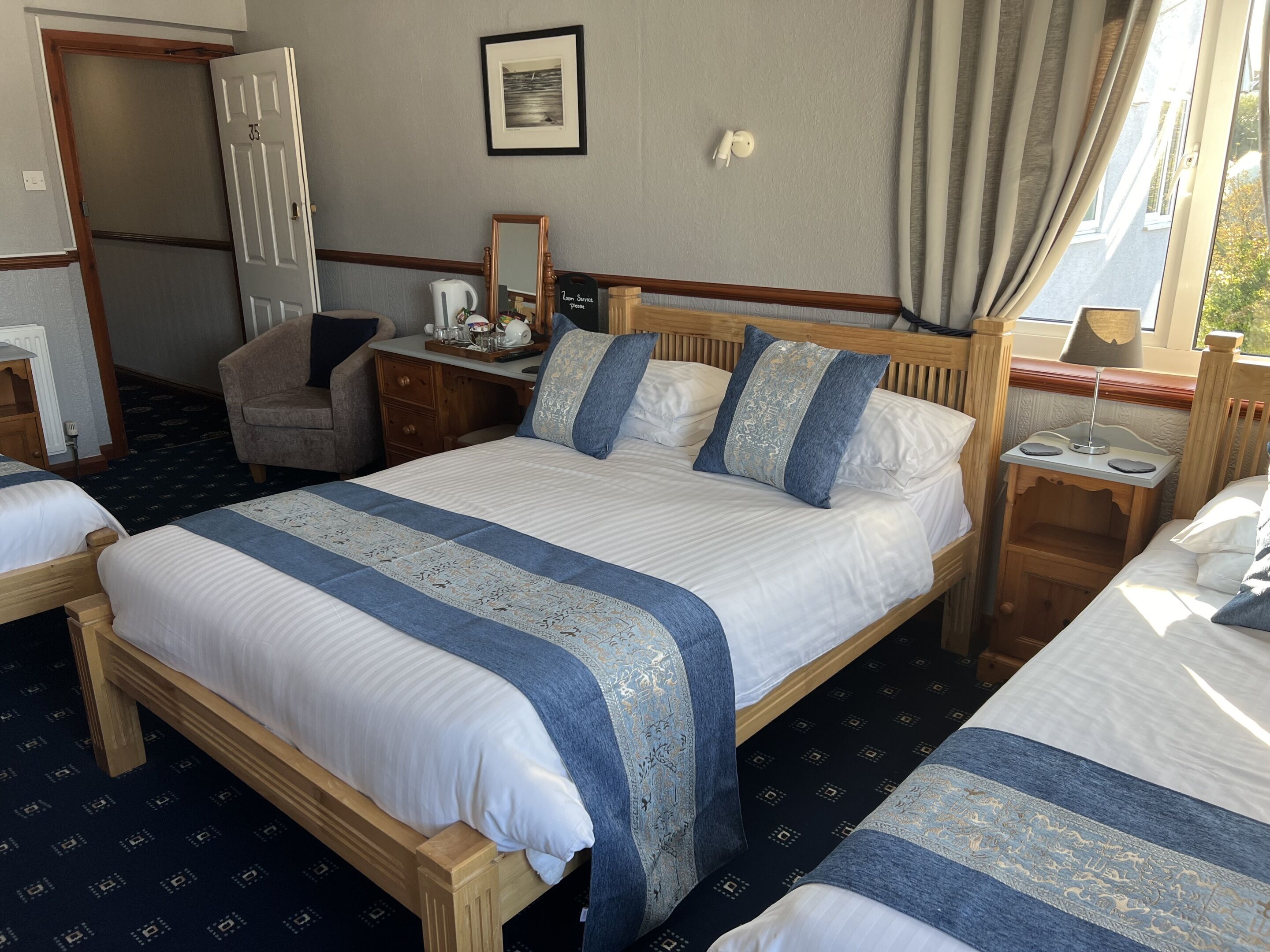 A hotel room with a large bed, a desk, a chair, a small table, a mirror, and a window with curtains.