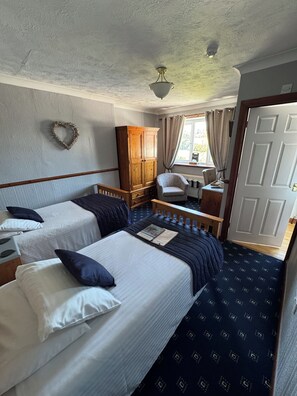 A room with two beds, a wardrobe, a chair, a small table, and a window with curtains.