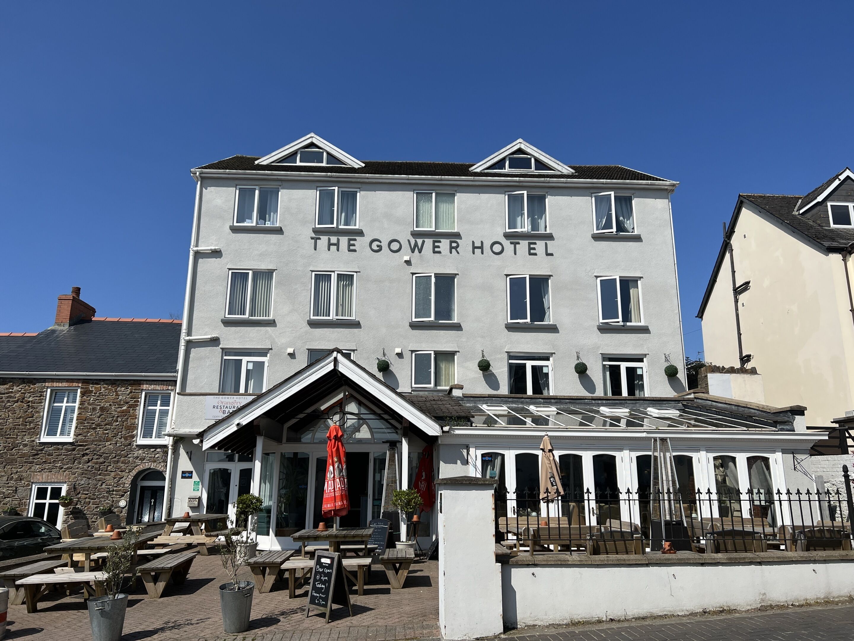 Un hôtel avec une enseigne indiquant « The Gower Hotel », des places assises à l’extérieur et un escalier menant à l’entrée.