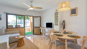 A modern living room with a sofa, coffee table, dining table with chairs, a television, and a ceiling fan. - Vacation Apartment 'Oasis Duna _ Casa Mate Pool' with Shared Pool, Private Terrace & Wi-Fi (Corralejo)