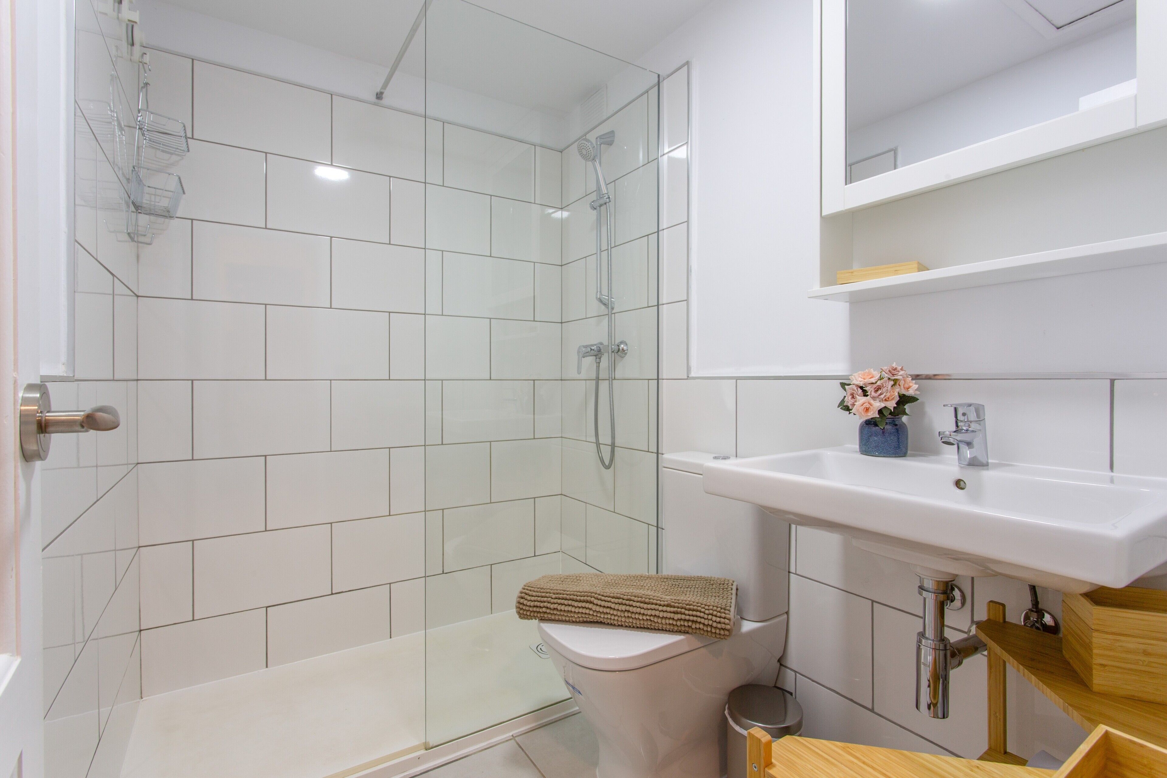 Ein modernes Badezimmer mit Duschkabine aus Glas, einer weißen Toilette und einem Waschbecken mit Blumen in einer Vase.