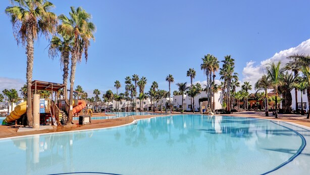 A swimming pool with palm trees, a water slide, and a covered area. - Vacation Apartment 'Oasis Duna _ Casa Mate Pool' with Shared Pool, Private Terrace & Wi-Fi (Corralejo)