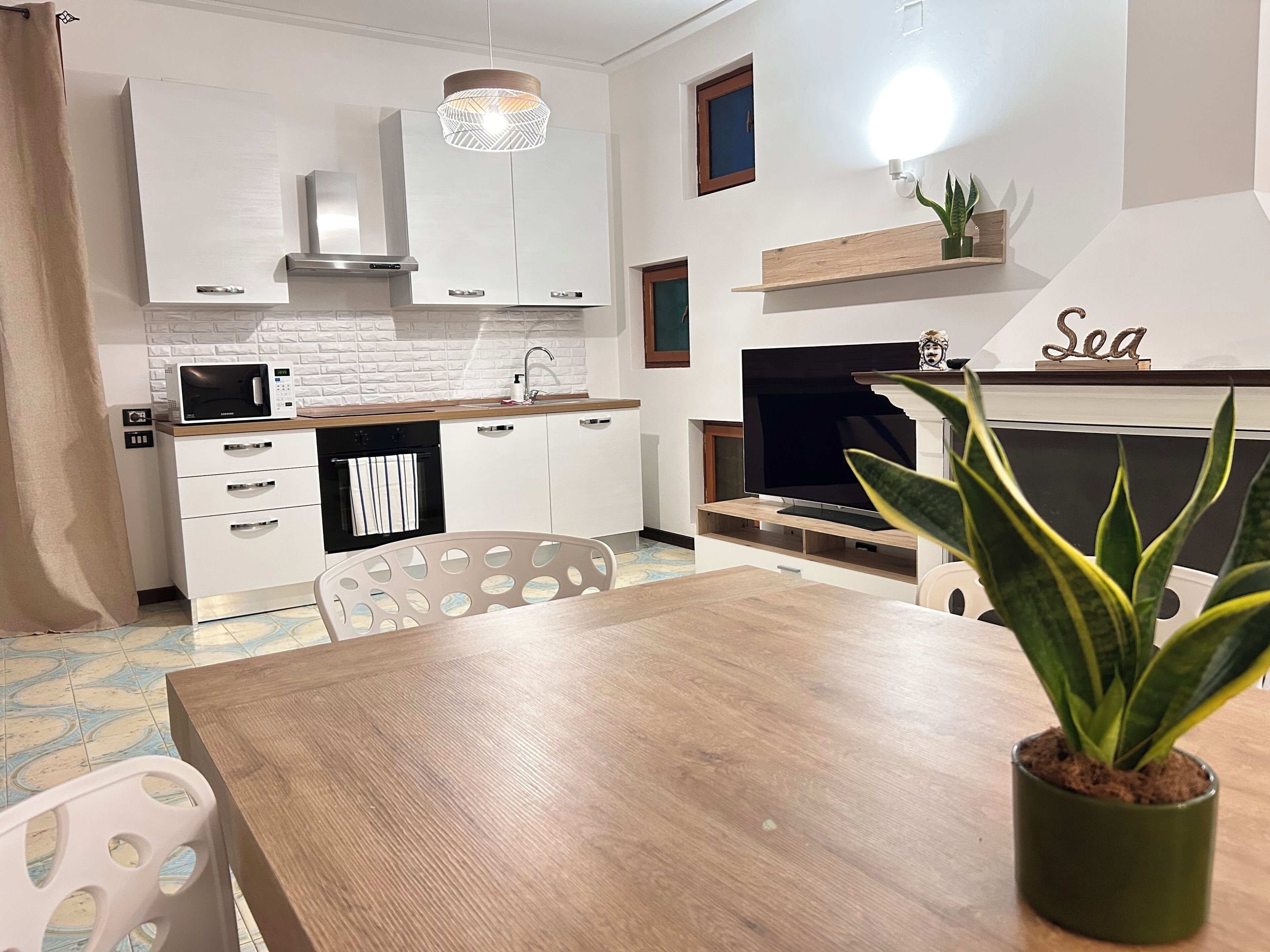 A modern kitchen with white cabinetry, a microwave, and a dining area with a wooden table and chairs.