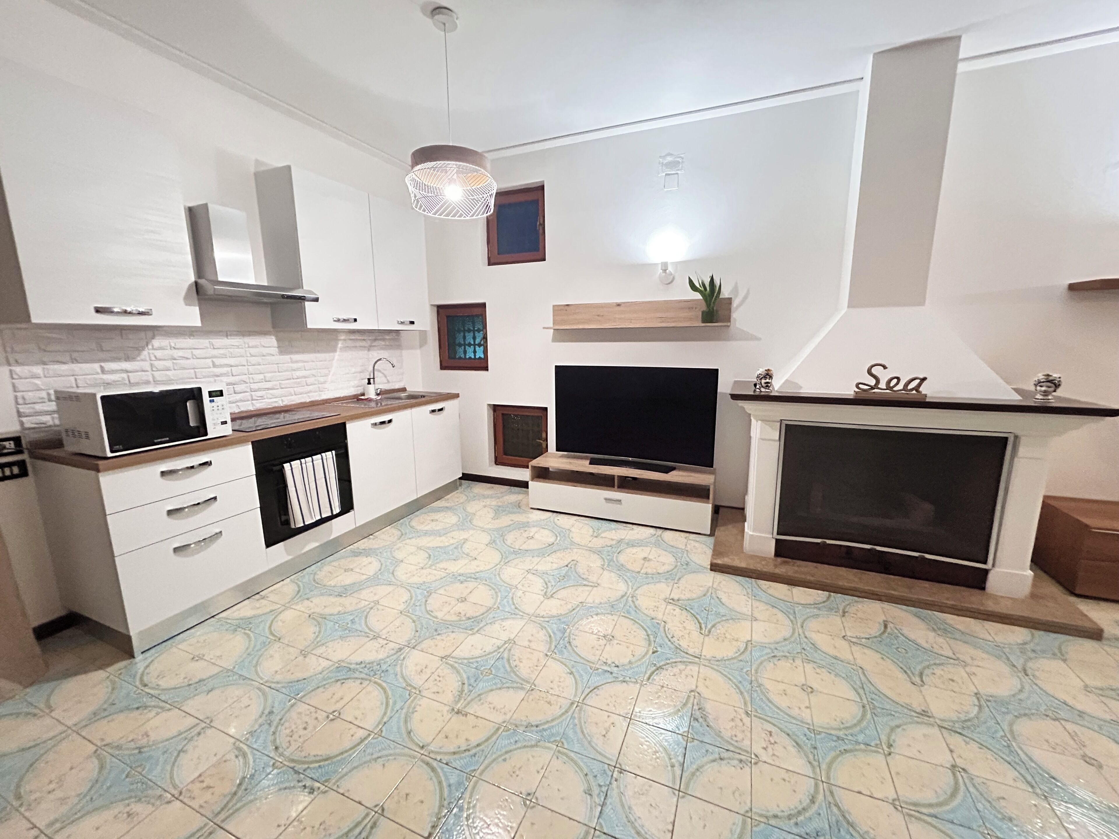 A modern kitchen with white cabinets, a microwave, a sink, and a television.