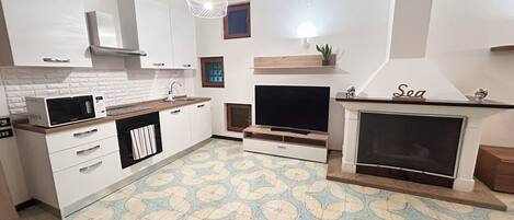A modern kitchen with white cabinets, a microwave, a sink, and a television.