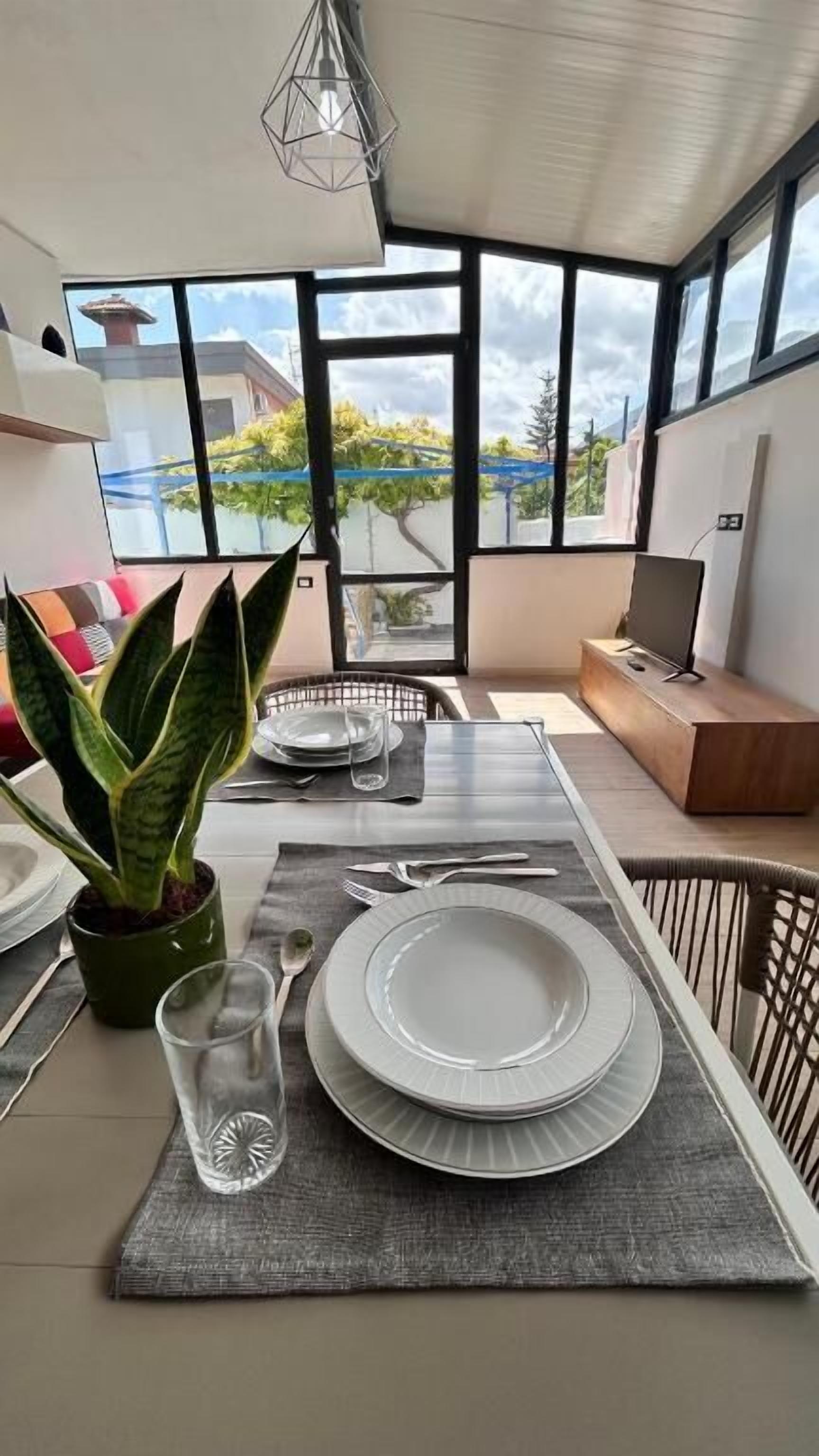 A dining area with a table set for two, a potted plant, and a view of the outdoors.