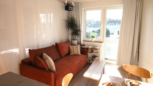A living room with a sofa, a coffee table, a dining table with chairs, a potted plant, and a view through a window. - High standard + private cinema & PS4 + close to Old Town (Warszawa)