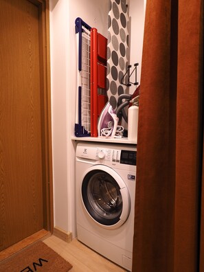 Un espace dédié à la lessive, comprenant un lave-linge, un étendoir et un rideau.