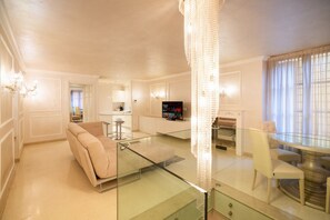 A modern living room with a glass coffee table, a beige sofa, a TV, and a chandelier. - Historic, elegant and modern residence on 3 floors (Verona)