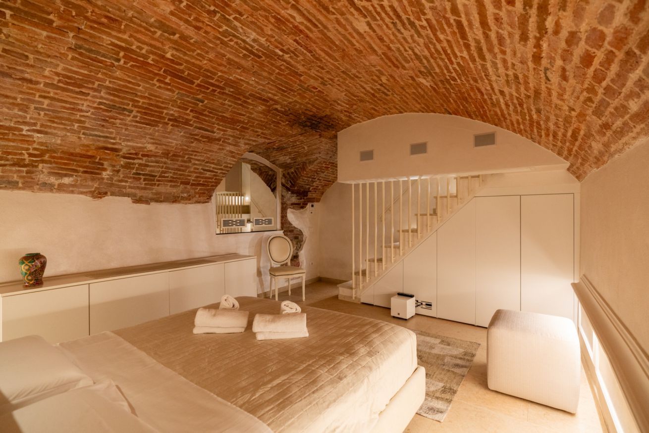 Ein Schlafzimmer mit Ziegeldecke, einem Bett mit Handtüchern, einem Schreibtisch, einem Stuhl und einer Treppe.