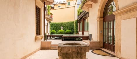 Un patio con un pozo de piedra en el centro, una pequeña piscina y un seto.