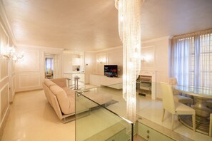 Ein modernes Wohnzimmer mit einem Glastisch, einem beigen Sofa, einem Fernseher und einer Chandelier.