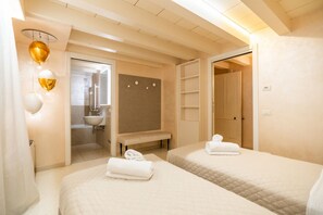 A hotel room with two beds, a bench, a bathroom with a sink, and a shower. - Historic, elegant and modern residence on 3 floors (Verona)