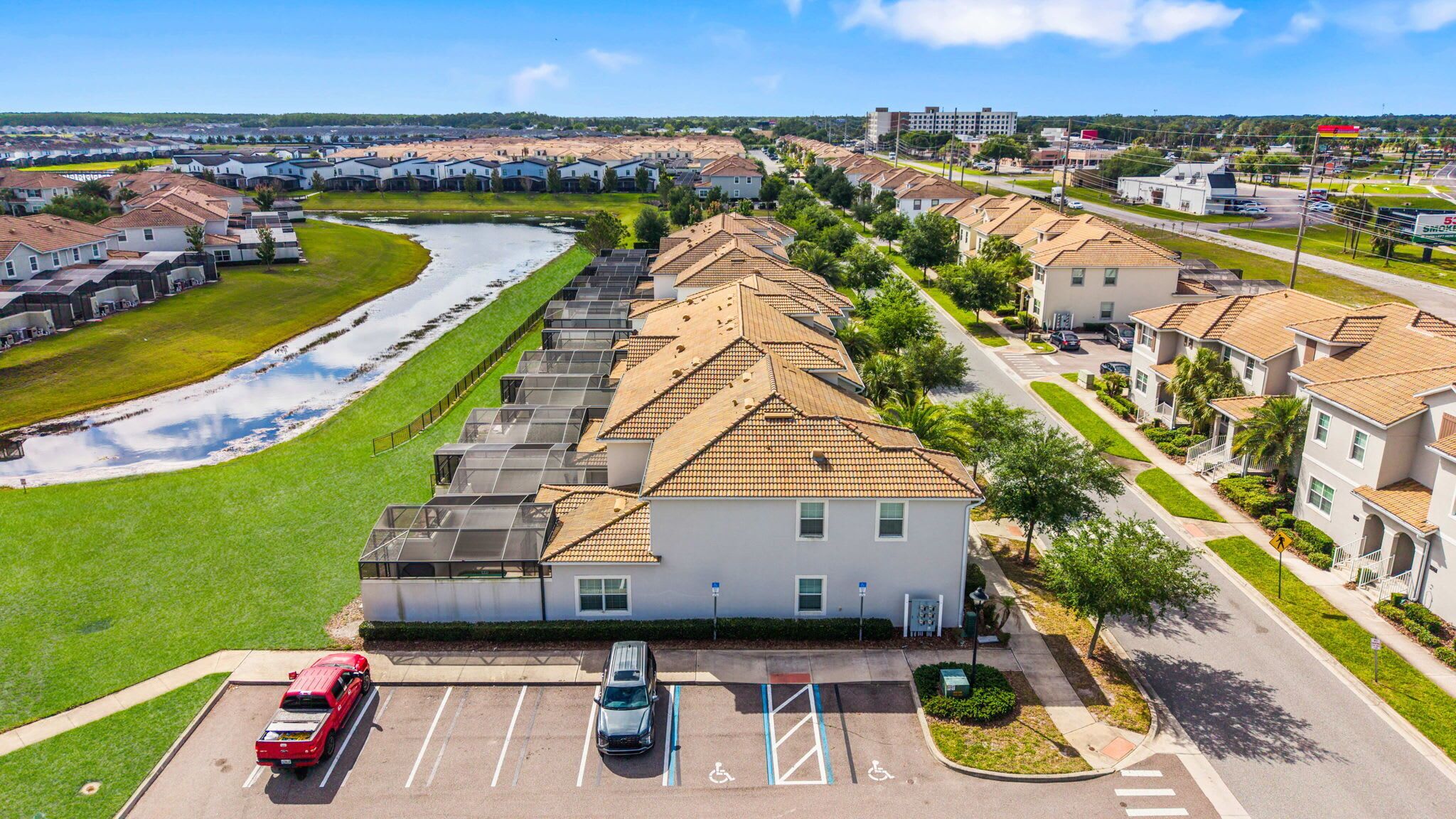 A residential area with a row of houses, a parking lot with cars, and a small body of water.