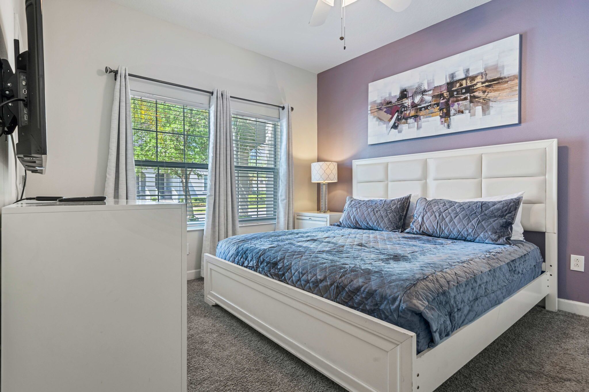 A bedroom with a bed, a TV, a window with curtains, and a painting on the wall.