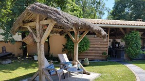 A wooden structure with a thatched roof, two lounge chairs, a small table, and a grill. - “Le Nid’zen” Guest Room with Wi-Fi (Le Nizan)
