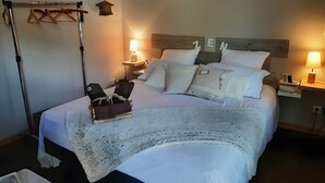 A neatly made bed with pillows and a blanket, a bedside table with a lamp, a wall-mounted shelf with a phone, and a relaxation chair with a rope. - “Le Nid’zen” Guest Room with Wi-Fi (Le Nizan)