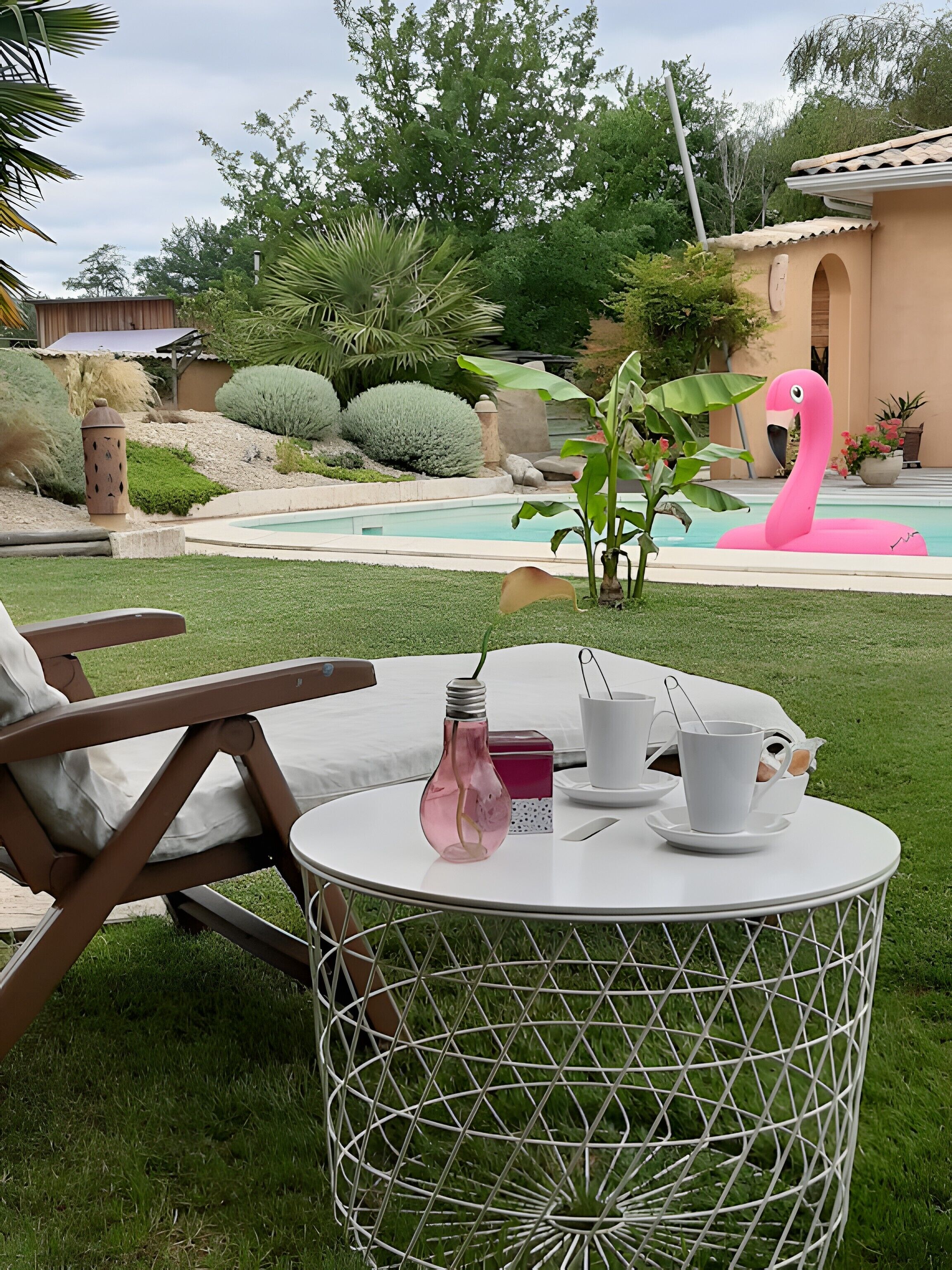 A round table with a white wireframe design, a pink flamingo float in a pool, and a patio chair.