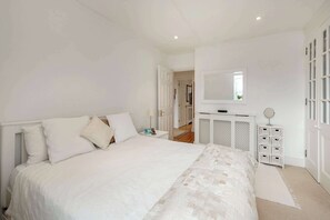 A bedroom with a large bed, a bedside table, a dresser, a mirror, and a door leading to another room. - Modern 2 bed Roof Terrace Flat - Earls Court (London)