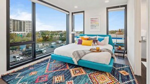 A modern bedroom with a large bed, a colorful rug, and large windows offering a city view. - New Walk to Gulch - Private Penthouse Pool Deck Views (Nashville)