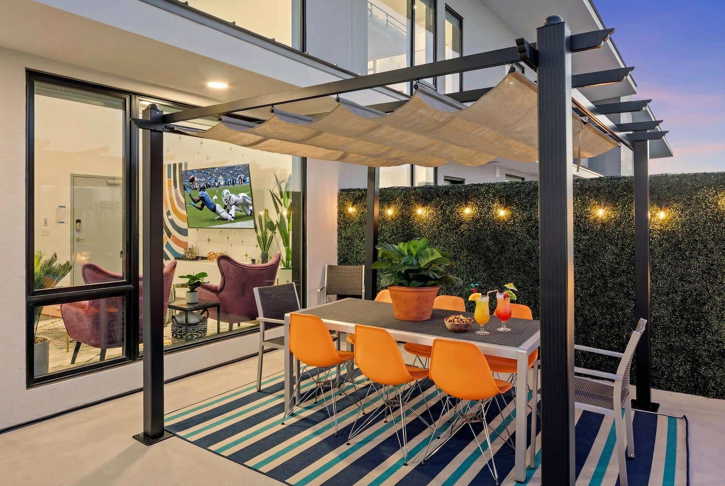 Un patio al aire libre con una mesa, sillas, una pérgola y un muro de setos.