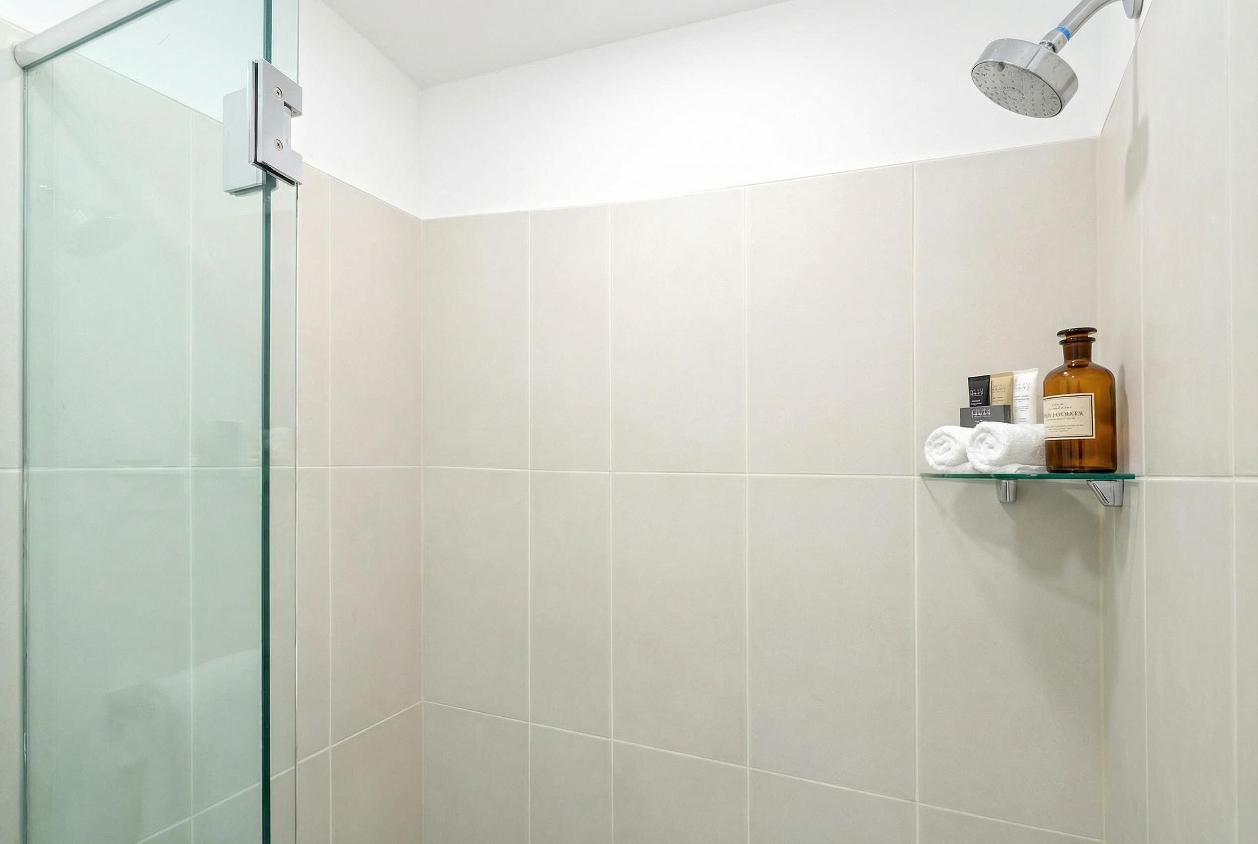 A shower with a glass door, a shelf with toiletries, and a showerhead.