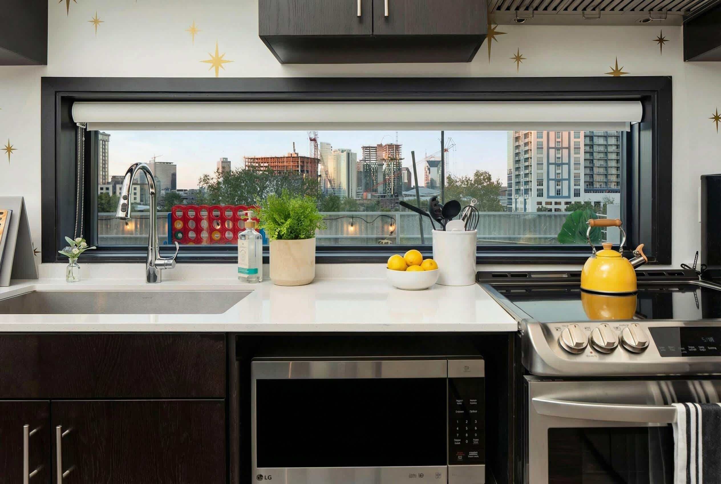 A modern kitchen with a dishwasher, stove, and sink, a window with a city view, and decorative items on the counter.