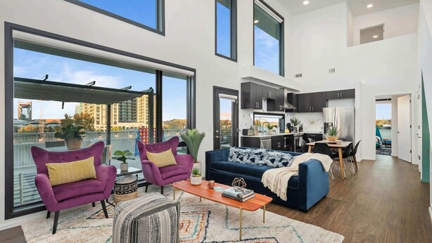 A spacious living area with a large window, a sofa, a coffee table, and a dining area. - New Walk to Gulch - Private Penthouse Pool Deck Views (Nashville)