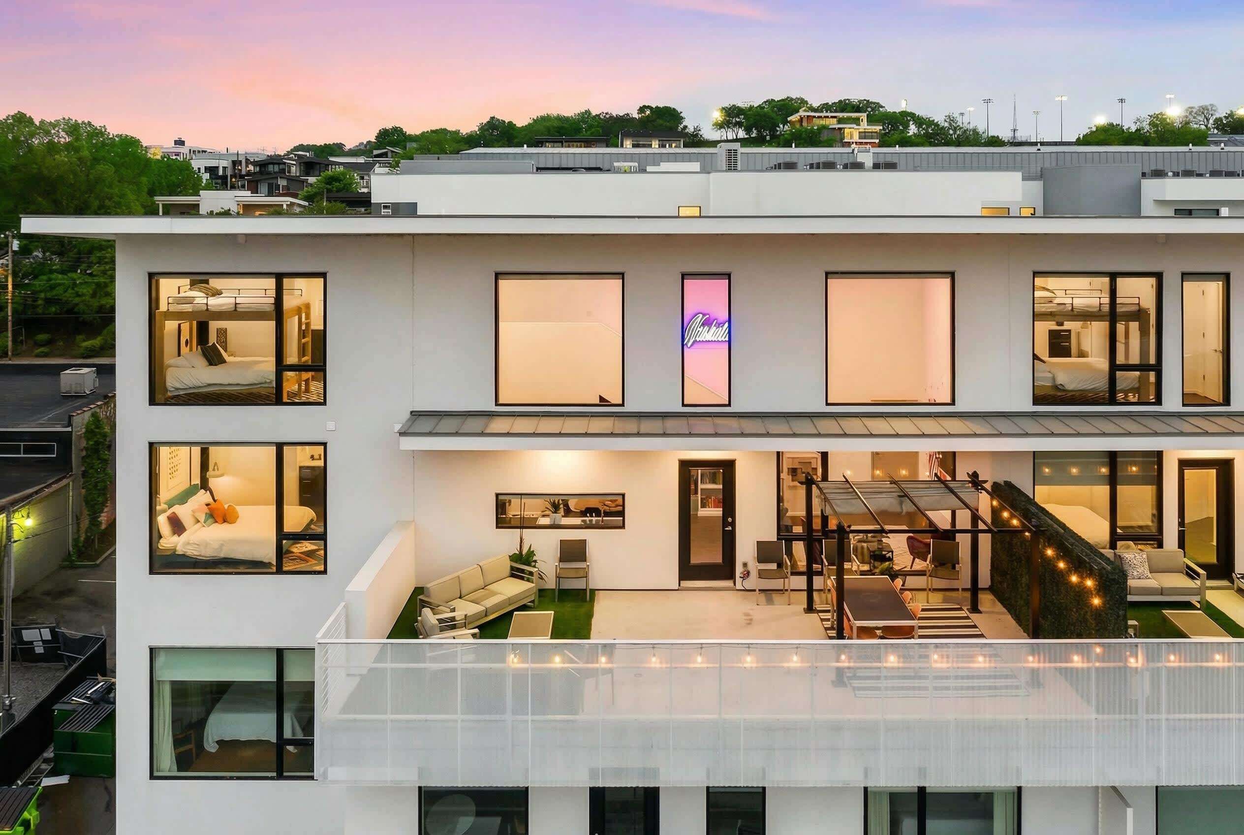 A modern multi-story hotel with a rooftop terrace, large windows, and a neon sign.