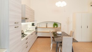 Moderni keittiö, jossa on valkoiset kaapit, ruokapöytä tuoleineen ja riippuvalaisin.