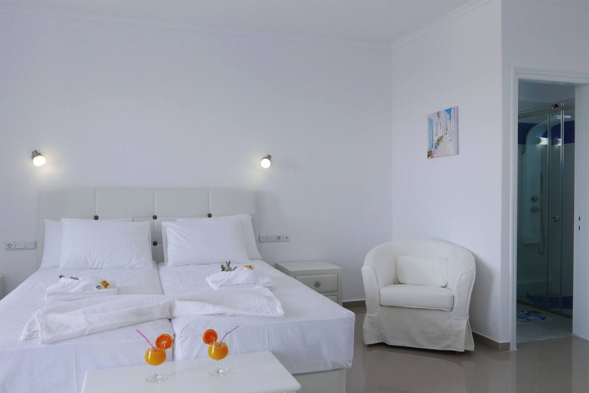 A hotel room with a large bed, two bedside tables, a chair, and a small table with two drinks.