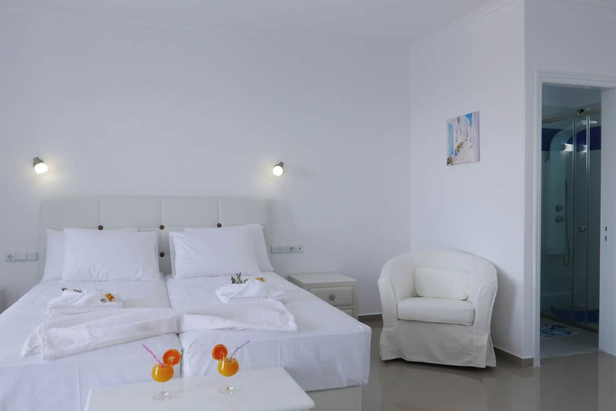 Une chambre d’hôtel avec un grand lit, deux tables de chevet, une chaise et une petite table sur laquelle sont posées deux boissons.