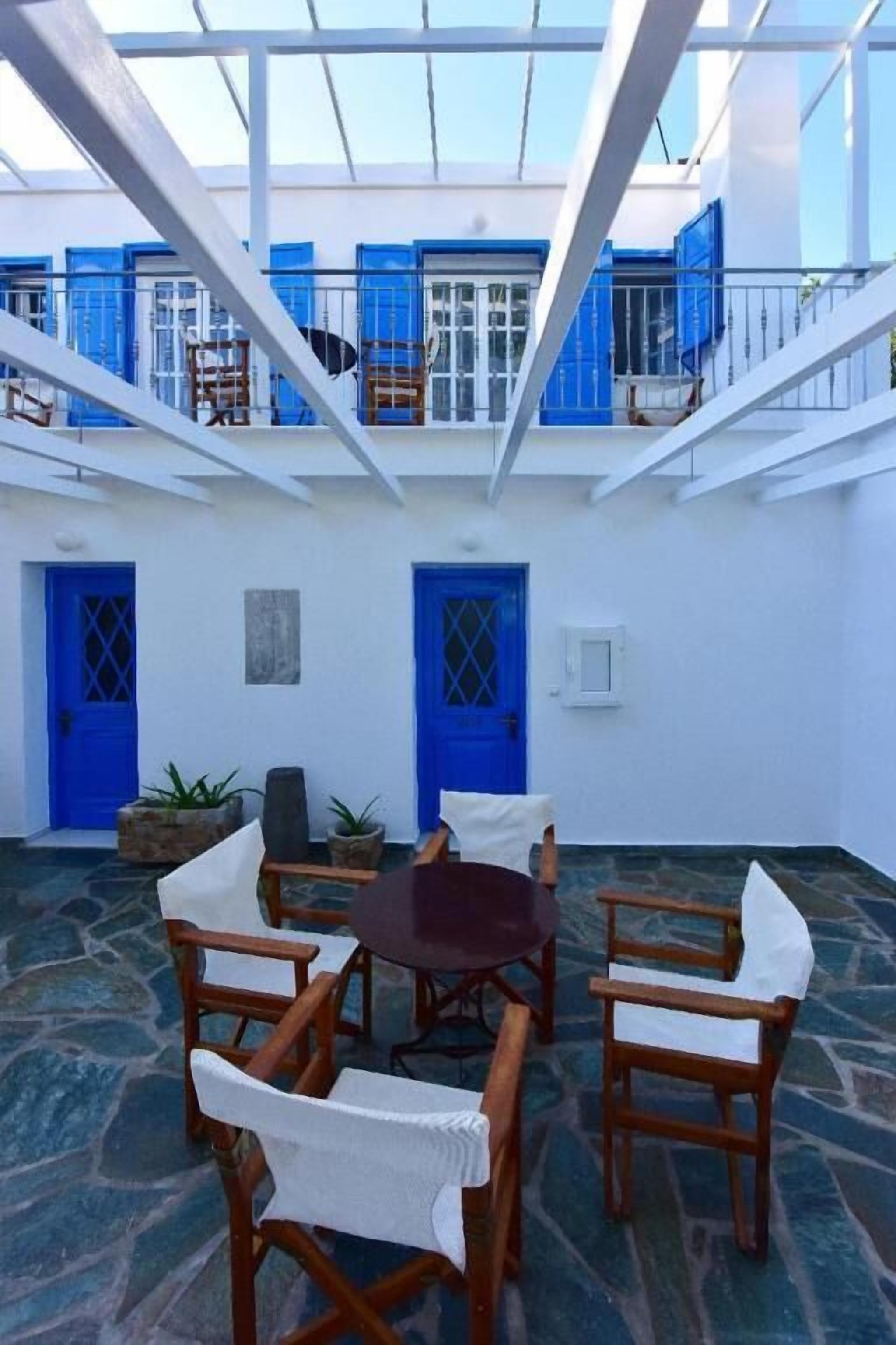 A courtyard with a round table and chairs, blue doors, and a white building with balconies.