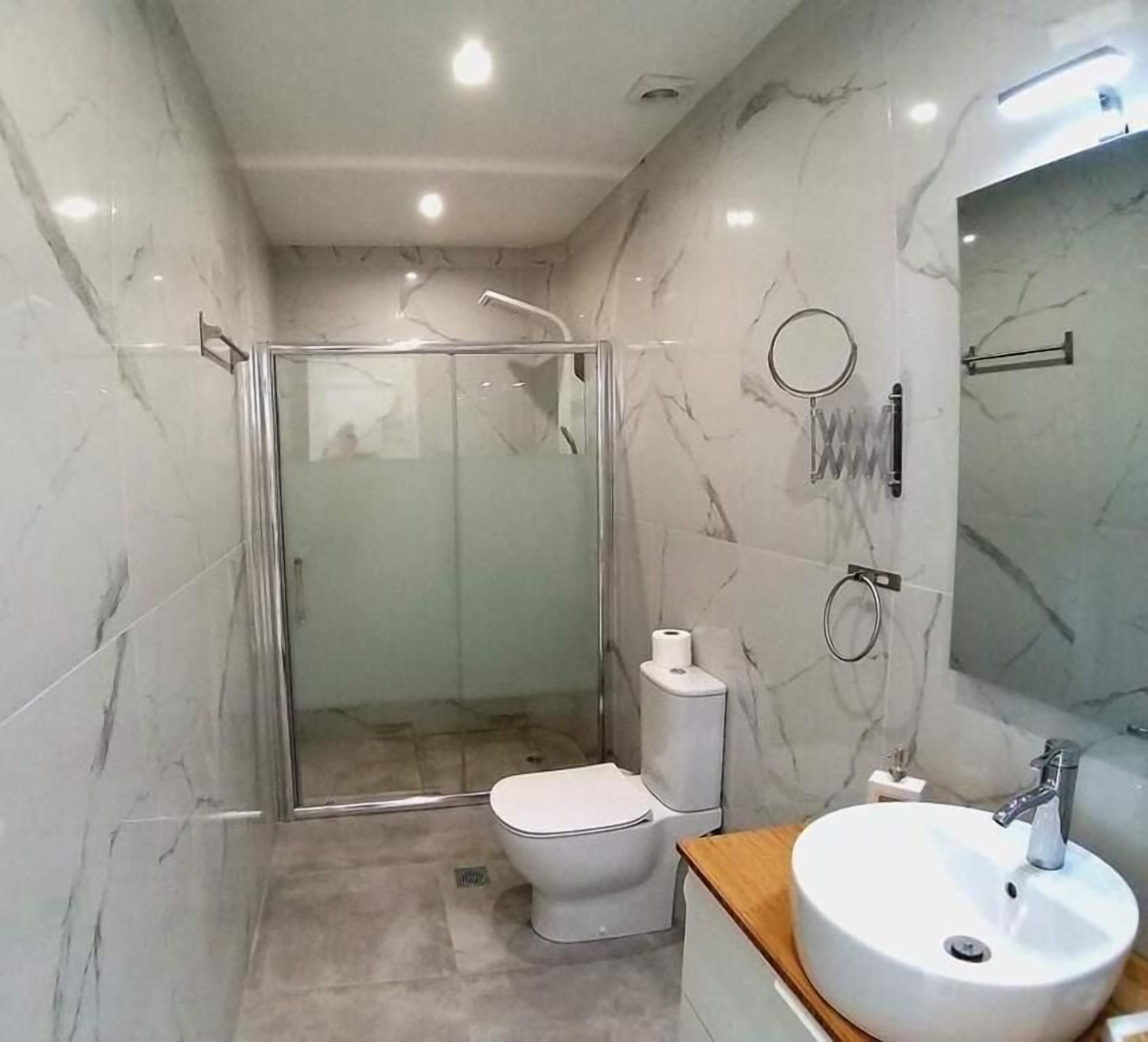 A modern bathroom with a glass-enclosed shower, a toilet, and a sink with a mirror.