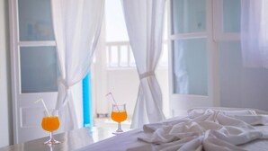 Una habitación de hotel con una cama, dos bebidas sobre una mesa y cortinas.