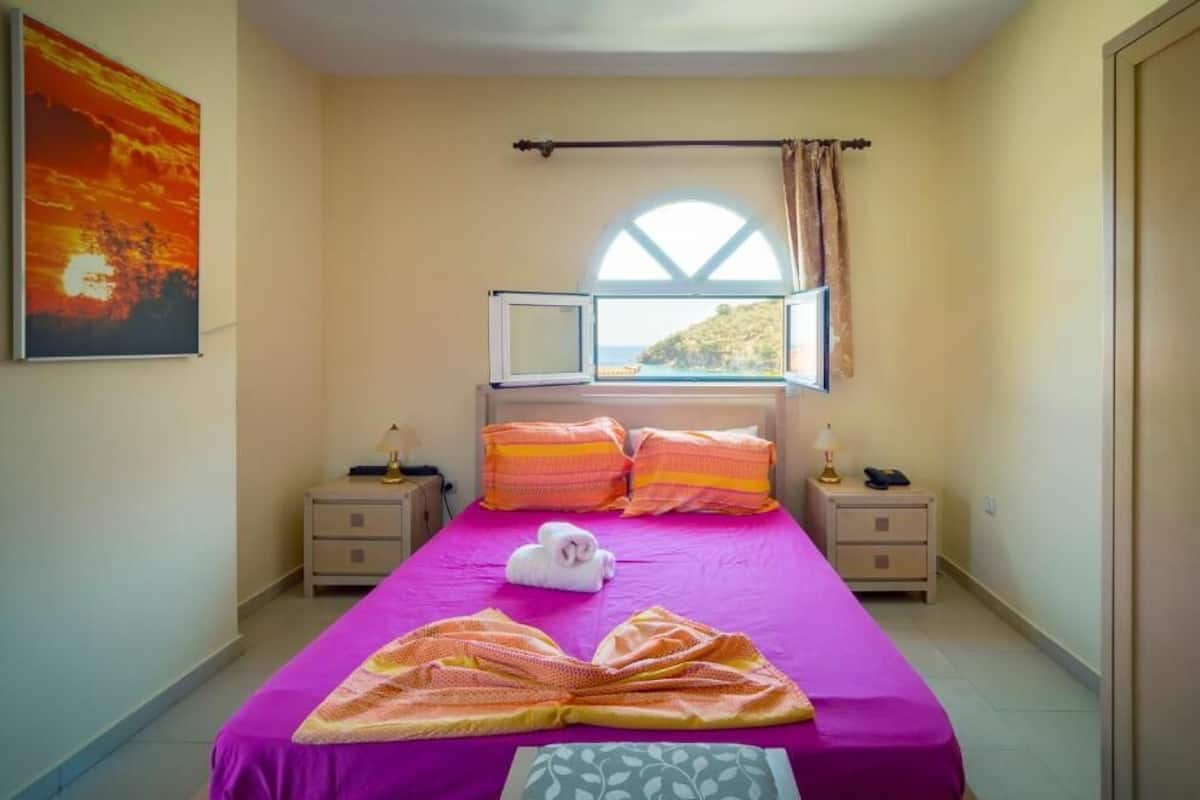 A bedroom with a bed, a window, a nightstand, a lamp, and a painting on the wall.