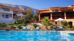 Un hotel con piscina, varios balcones y montañas al fondo.