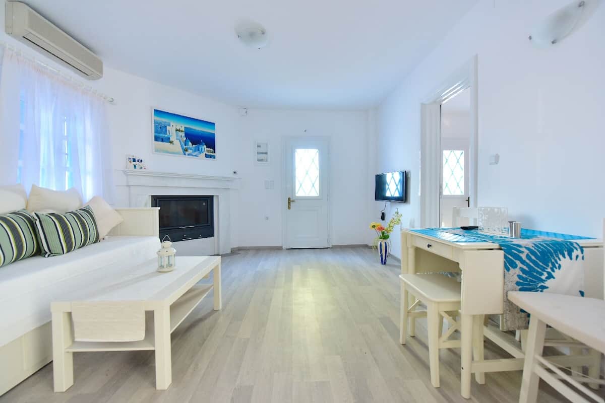 A room with a sofa, a TV, a fireplace, a dining table, and a TV on the wall.