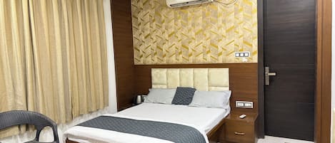 A bedroom with a bed, a chair, a ceiling fan, an air conditioner, a wooden door, and a patterned wall.