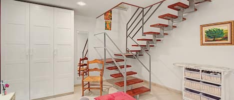 Un dormitorio con cama, una silla de madera, un armario blanco, una escalera y un mueble de almacenamiento de mimbre.