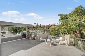 Eine Dachterrasse mit Sitzgelegenheiten im Freien, Palmen und Blick auf die Stadt.
