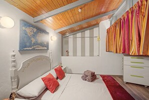 Une chambre avec un plafond en bois, une carte du monde accrochée au mur, un lit avec des oreillers rouges, une petite table sur laquelle est posée une figurine, et un rideau à rayures.