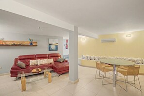 A living room with a red leather sofa, a glass coffee table, and a dining area with wicker chairs and a glass table.