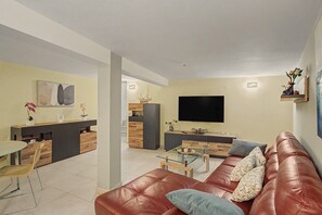 A modern living room with a leather sofa, a glass coffee table, and a flat-screen TV mounted on the wall.