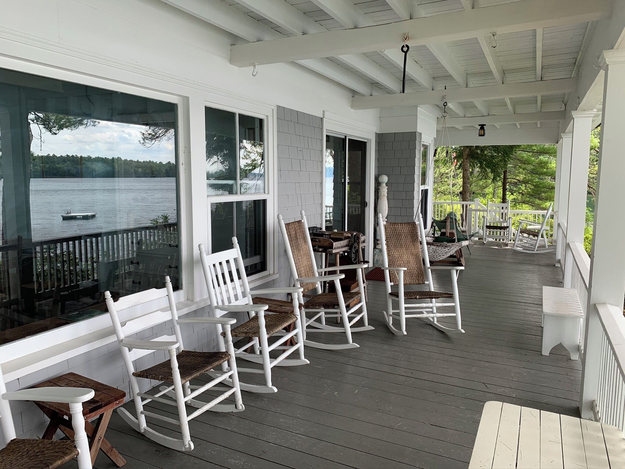 A covered porch with white rocking chairs and a view of a lake.