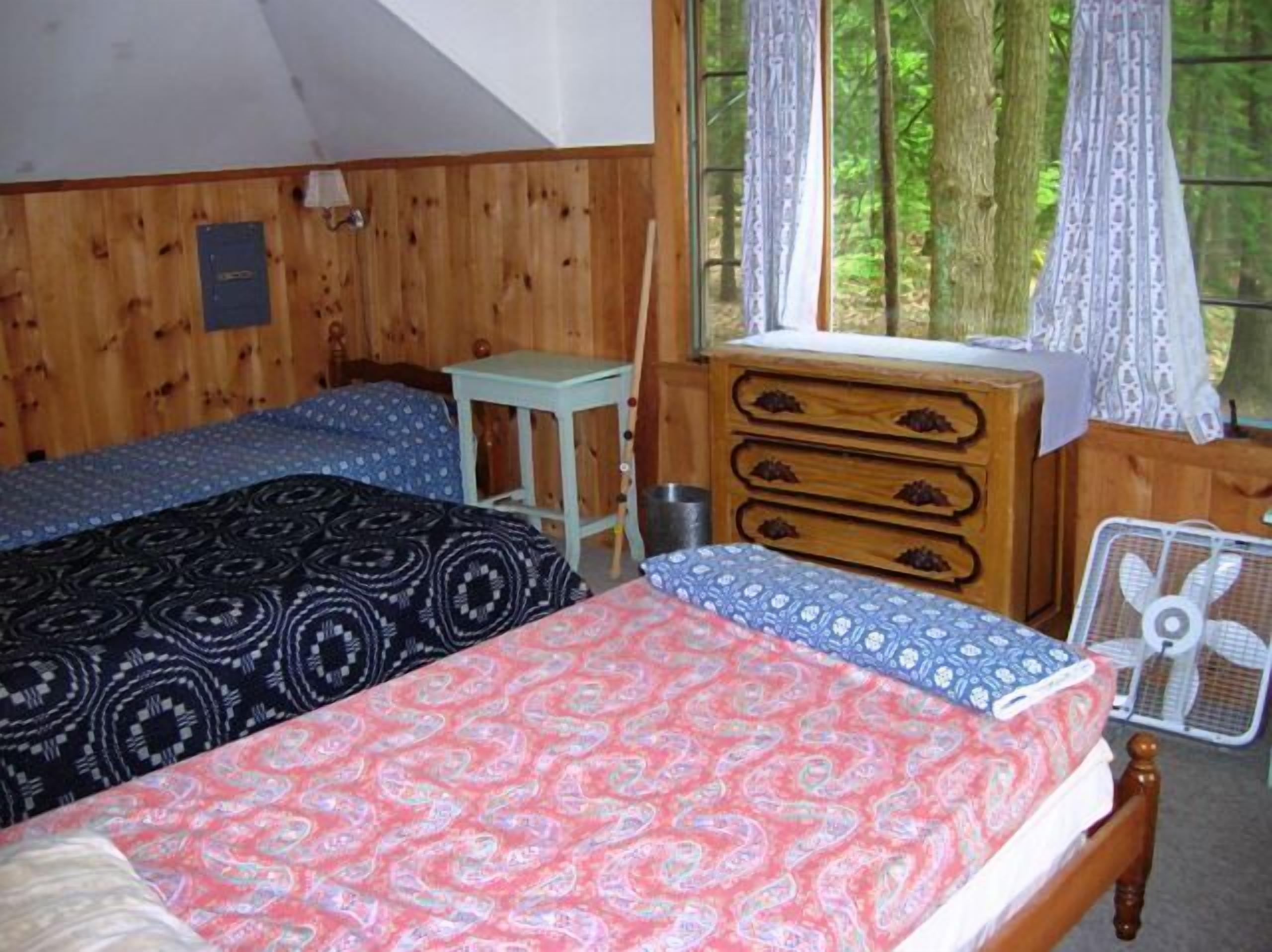 Een kamer met een bed, een dressoir, een klein tafeltje en een raam met gordijnen.