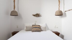 Ein Bett mit weißer Bettwäsche, zwei Körbe, die von der Decke hängen, und eine Holzdeko an der Wand.