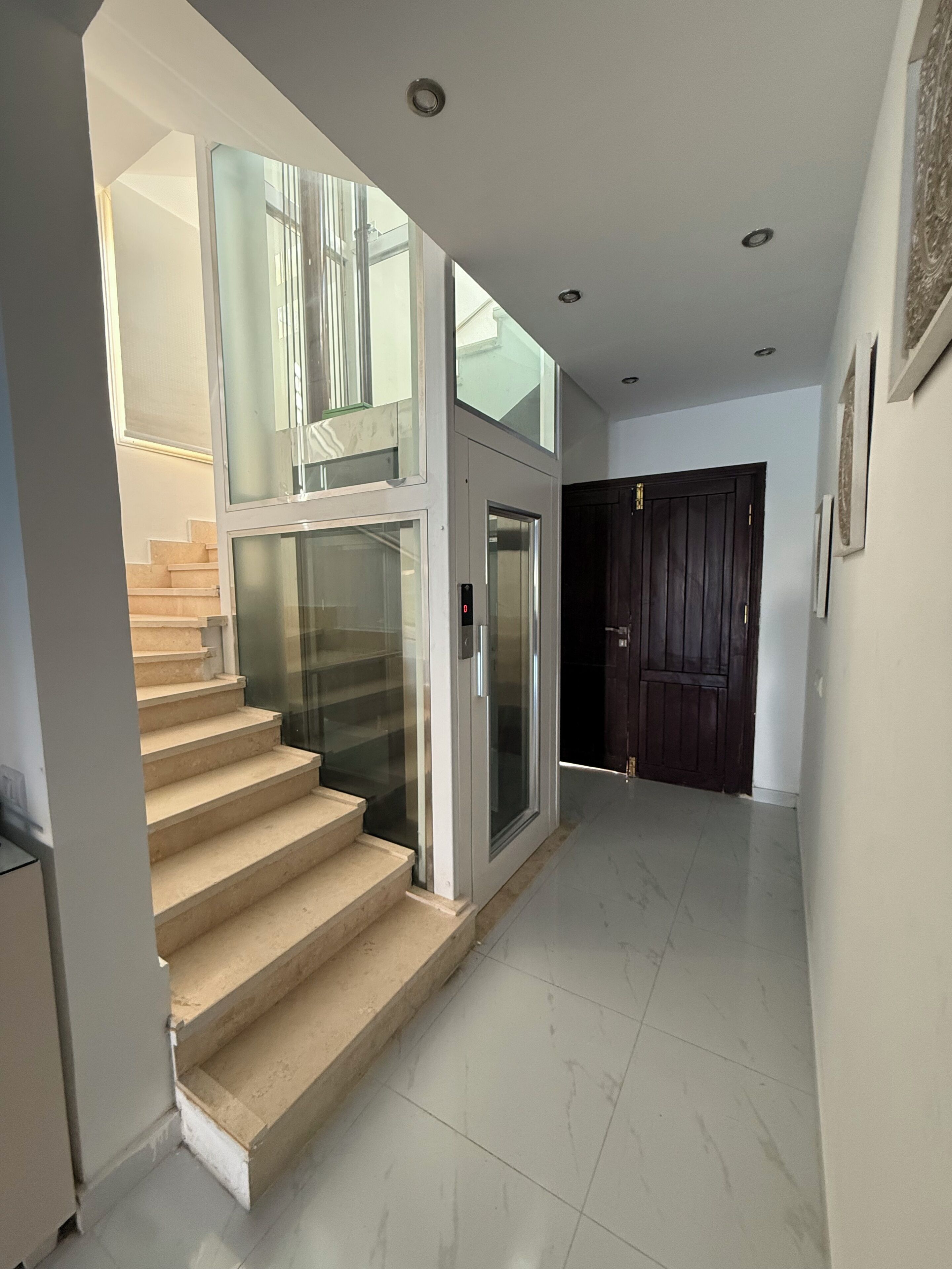 A modern interior with a glass staircase, a door, and a tiled floor.