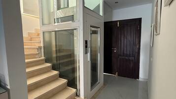 A modern interior with a glass staircase, a door, and a tiled floor.